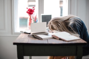 person with head on desk surrounded by books